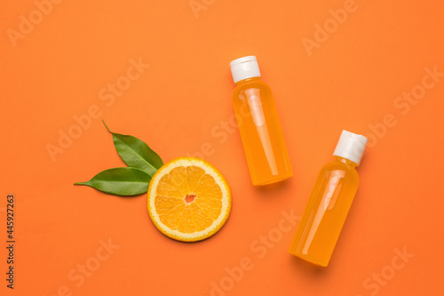 A piece of orange with leaves and two bottles of juice on an orange background. Flat lay.