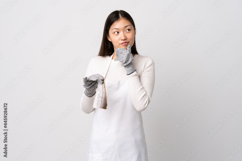 Chinese fishmonger wearing an apron and holding a raw fish over isolated white background thinking an idea while looking up Chinese fishmonger wearing an apron and holding a raw fish over isolated white background thinking an idea while looking up