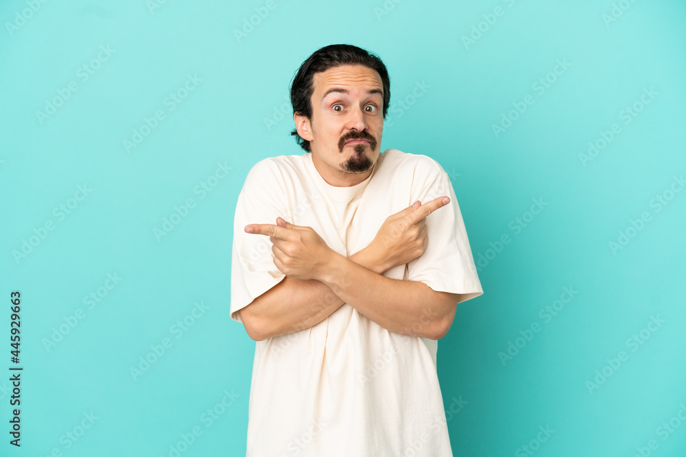 Young caucasian man isolated on blue background pointing to the laterals having doubts Young caucasian man isolated on blue background pointing to the laterals having doubts