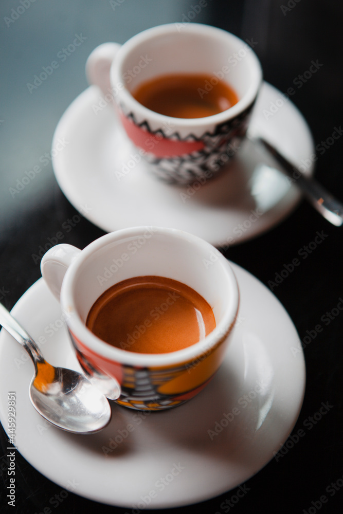 Traditional Italian coffee. Two small colorful espresso cups on a white  saucer with a spoon on a black table at the bar in Milan, Lombardy, Italy.  European beverages and drinks. Stock Photo