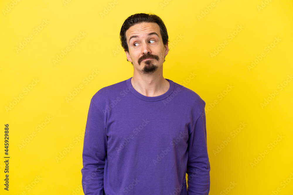 Young caucasian man isolated on yellow background making doubts gesture looking side Young caucasian man isolated on yellow background making doubts gesture looking side
