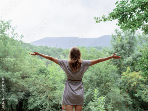 Young woman in summer dress standing on a big rock in the forest looking away