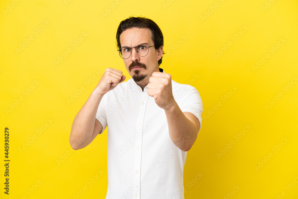 Young caucasian man isolated on yellow background with fighting gesture Young caucasian man isolated on yellow background with fighting gesture