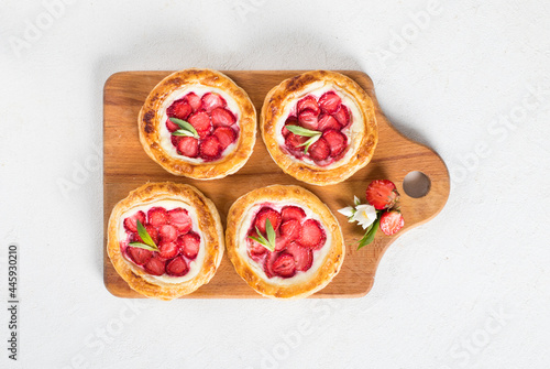 Mini open pies made of puff pastry with ricotta and fresh strawberries on a wooden board on a white background top view
