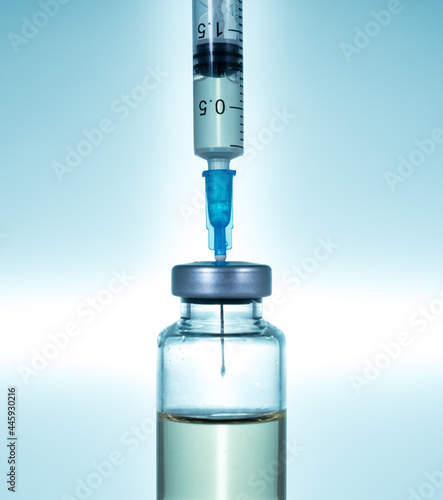 Macro of a hypodermic syringe or needle being filled with vaccine from bottle against a blue star background