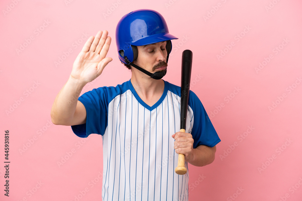 Young caucasian man playing baseball isolated on pink background making stop gesture and disappointed