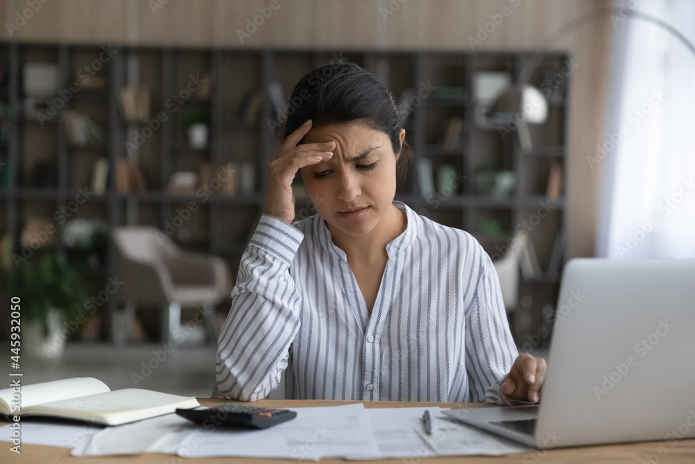 Fototapeta premium Unhappy young Indian woman distressed with debt or bankruptcy managing household finances or budget. Upset ethnic female frustrated with financial problems calculating expenses paying online.
