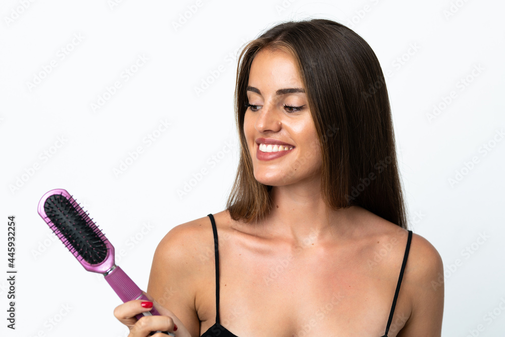Young Uruguayan woman isolated on white background with hair comb and looking it Young Uruguayan woman isolated on white background with hair comb and looking it