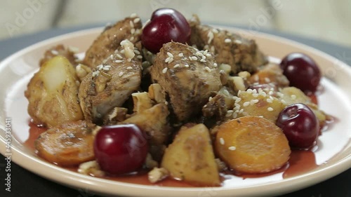 Jewish roast dish with chicken in cherry sauce on a plate decorated with cherries rotates in a circle photo