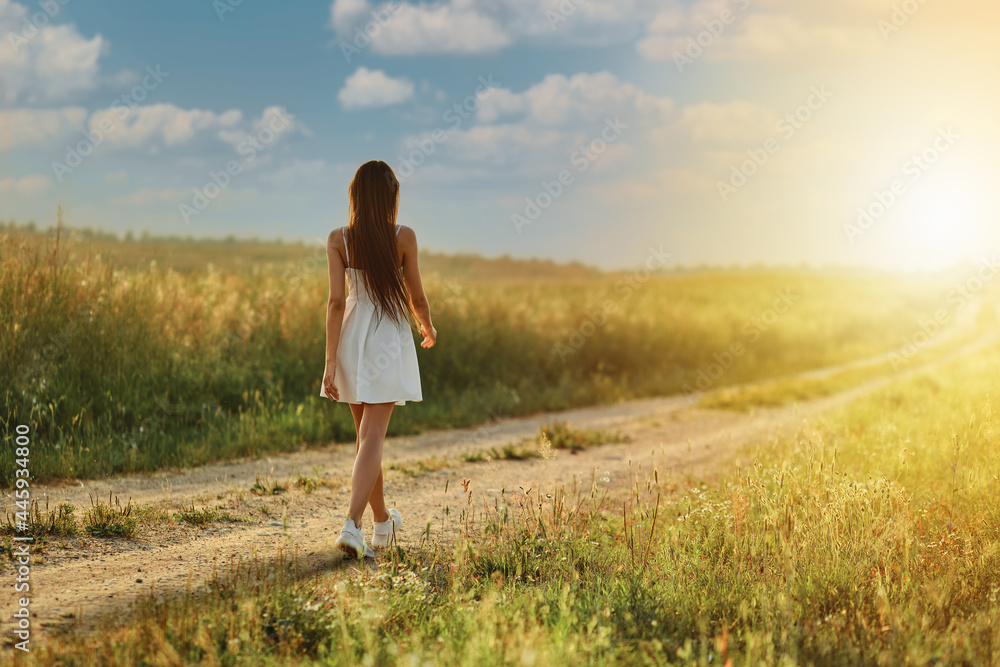 Rear view of a woman walking along country road in the meadow Rear view of a woman walking along country road in the meadow