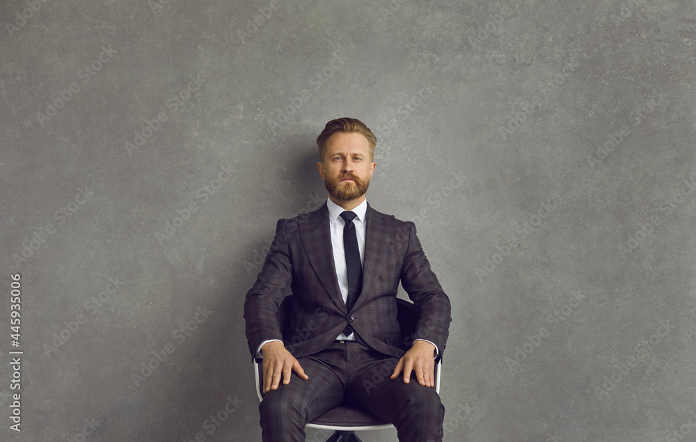 Portrait of confident sharp dressed bearded Caucasian businessman and professional business executive. Good looking man in classy elegant grey suit, white shirt and necktie sitting on chair in studio Portrait of confident sharp dressed bearded Caucasian businessman and professional business executive. Good looking man in classy elegant grey suit, white shirt and necktie sitting on chair in studio
