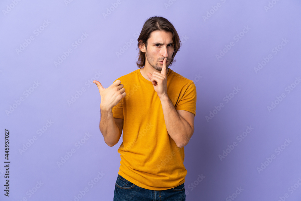Young handsome man isolated on purple background pointing to the side and doing silence gesture Young handsome man isolated on purple background pointing to the side and doing silence gesture