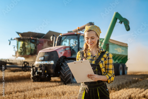 Farmer on grain field with tractor and combine harvester in background taking notes