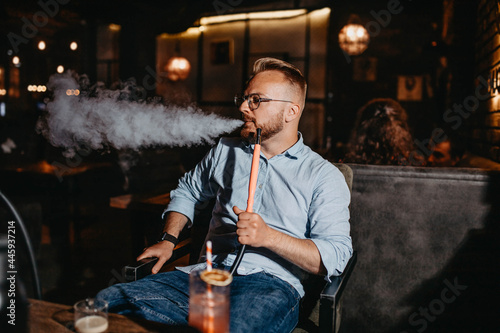 young man smokes a hookah in the evening in a hookah bar.
