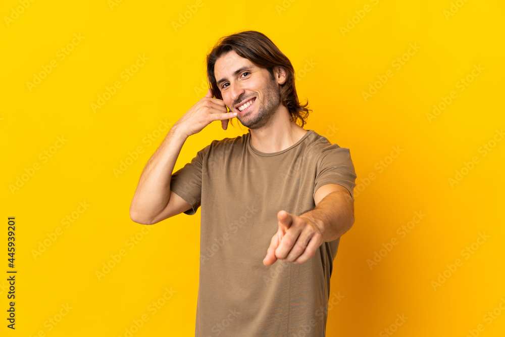 Young handsome man isolated on yellow background making phone gesture and pointing front Young handsome man isolated on yellow background making phone gesture and pointing front