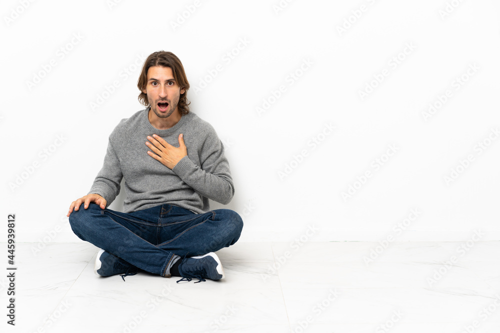 Young handsome man sitting on the floor over isolated background surprised and shocked while looking right Young handsome man sitting on the floor over isolated background surprised and shocked while looking right