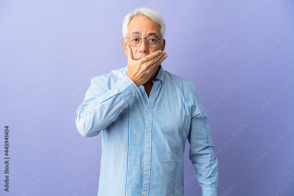 Middle age Brazilian man isolated on purple background covering mouth with hand