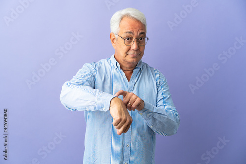 Middle age Brazilian man isolated on purple background making the gesture of being late © luismolinero
