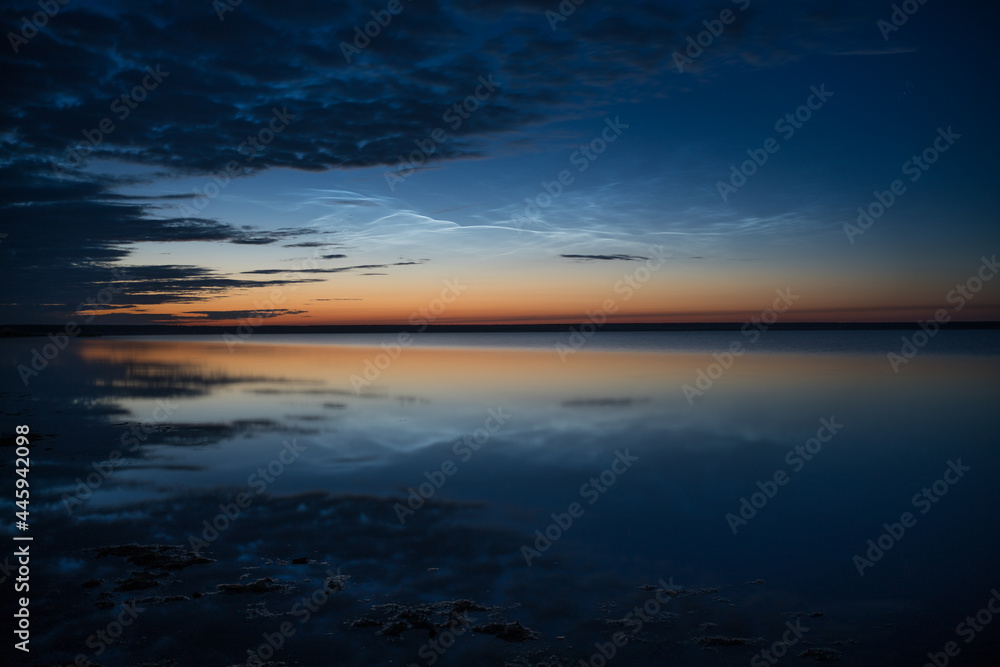 Noctilucent clouds on the background of the night sky with reflection in the water of the lake, natural phenomenon, beautiful nature background