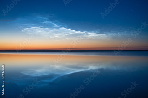 Noctilucent clouds on the background of the night sky with reflection in the water of the lake, natural phenomenon, beautiful nature background © gerasimov174