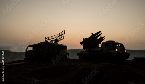 Creative artwork decoration. Silhouette of mobile air defence truck with radar antenna during sunset. Satellite dishes or radio antennas against evening sky.