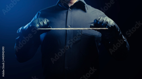 Photo of a shaded strangler assassin man in black shirt and leather gloves holding rope.