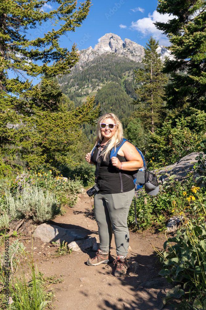 Naklejka premium Full body portrait of a smiling blonde female hiker on the trail at Grand Teton National Park