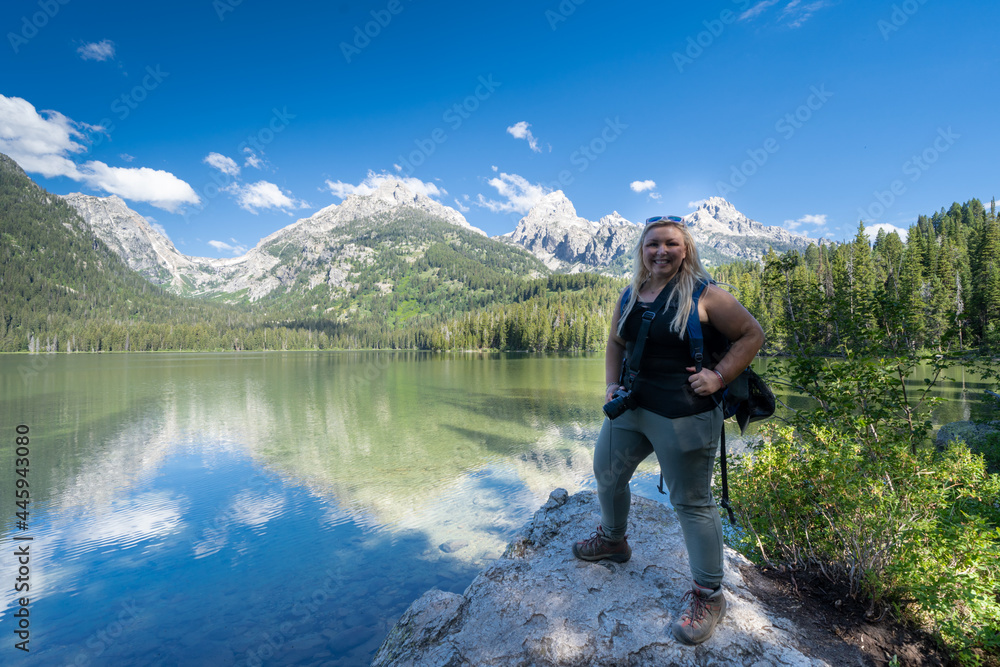 Proud blonde woman hiker stands on a rock on the shoreline of Taggart Lake, in Grand Teton National Park