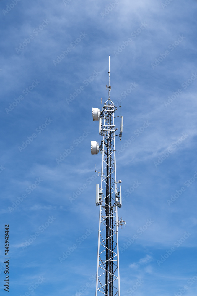 Modern wireless telecommunication tower antenna transmitter or base reciever station for broadcasting 4G or 5G cellular telephone, television, and Internet signals, against a blue sky.