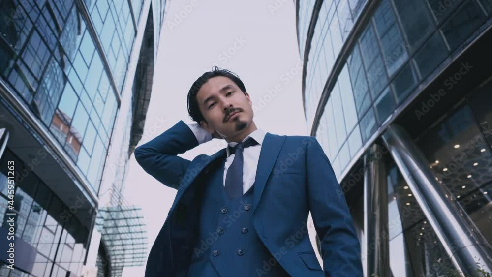 Shot of the well-dressed happy confident thoughtful businessman mixed wearing a suit and tie looking at the camera while standing near modern office building. Office corporate male executive. Shot of the well-dressed happy confident thoughtful businessman mixed wearing a suit and tie looking at the camera while standing near modern office building. Office corporate male executive.