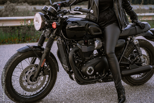 Legs of stylish motorcyclist woman sitting on classic bike. Black retro-styled motorcycle. Details of vintage design of brand-new motorbike. © kohanova1991
