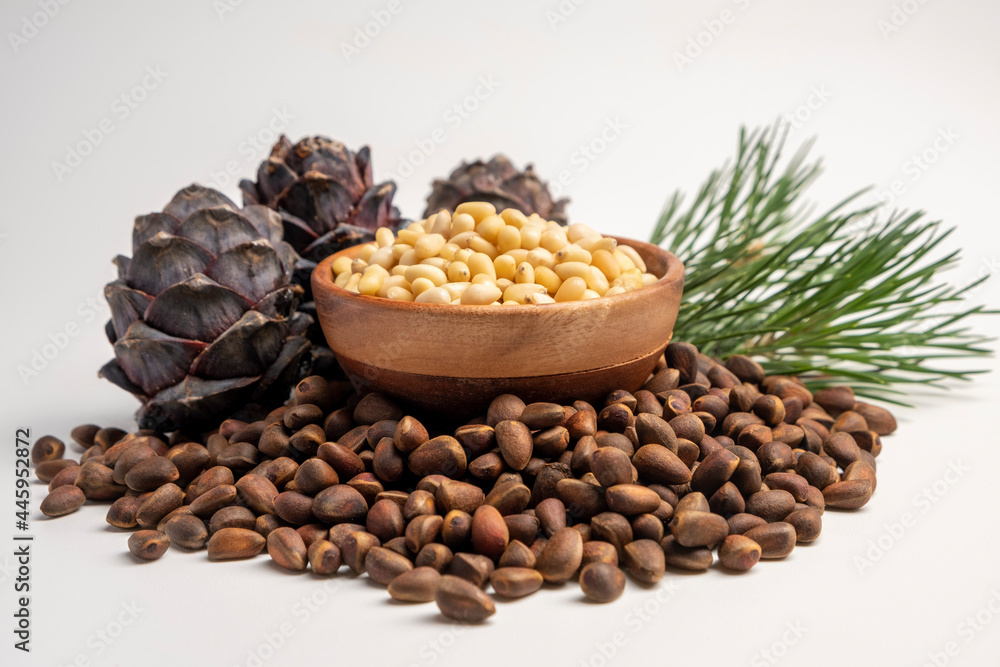 Pine nuts in wooden bowl with cones on white background Pine nuts in wooden bowl with cones on white background