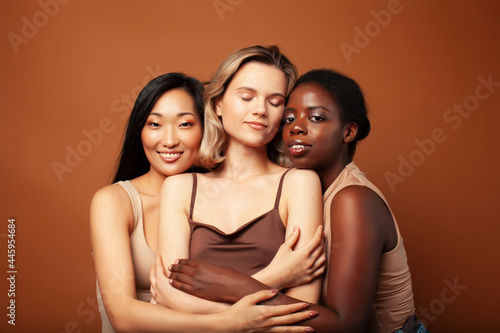 young pretty asian, caucasian, afro woman posing cheerful together on brown background, lifestyle diverse nationality people concept