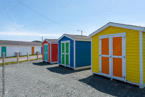 A row of small colorful painted huts or sheds made of wood. The exterior walls are colorful with double wooden doors. The sky is blue in the background and the storage units are sitting on gravel. © Dolores  Harvey
