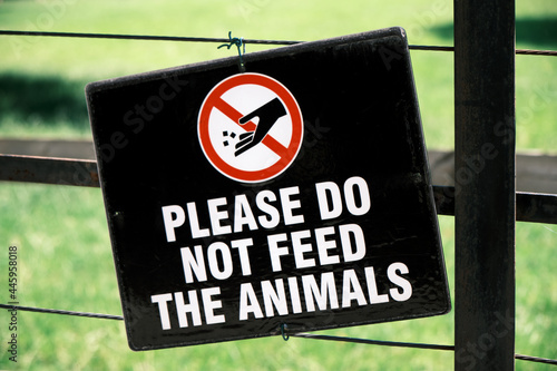 Close-up of Please Do Not Feed The Animals sign hung on a fence. Green grass in the background.