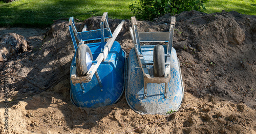 Two blue dirty wheelbarrows turned upside down in the dirt at a building construction site.