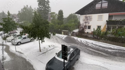 Environmental disaster, high water and tons of hails are flowing down the street in a little city with parking cars while it's still raining heavly. photo