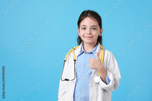 Obraz na plátne Little girl with stethoscope dressed as doctor on light blue background, space for text
