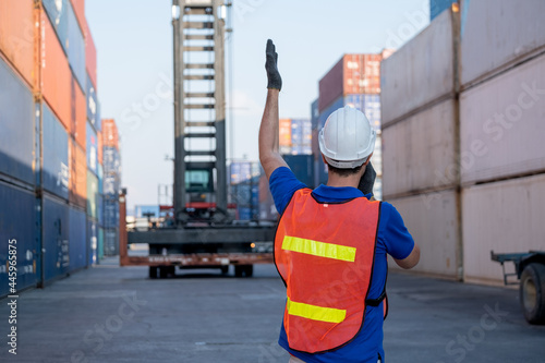 Back of foreman or cargo container worker give hand signal to crane movement in workplace area. Concept of teamwork support for delivery factory business system.