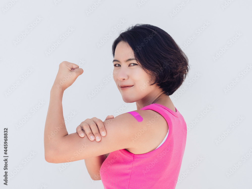 Vaccinations, bandage on vaccinated people concept. Confident Asian woman in pink tank top showing bandage plaster showing strong gesture with fist hand after vaccination treatment isolated on white. Vaccinations, bandage on vaccinated people concept. Confident Asian woman in pink tank top showing bandage plaster showing strong gesture with fist hand after vaccination treatment isolated on white.