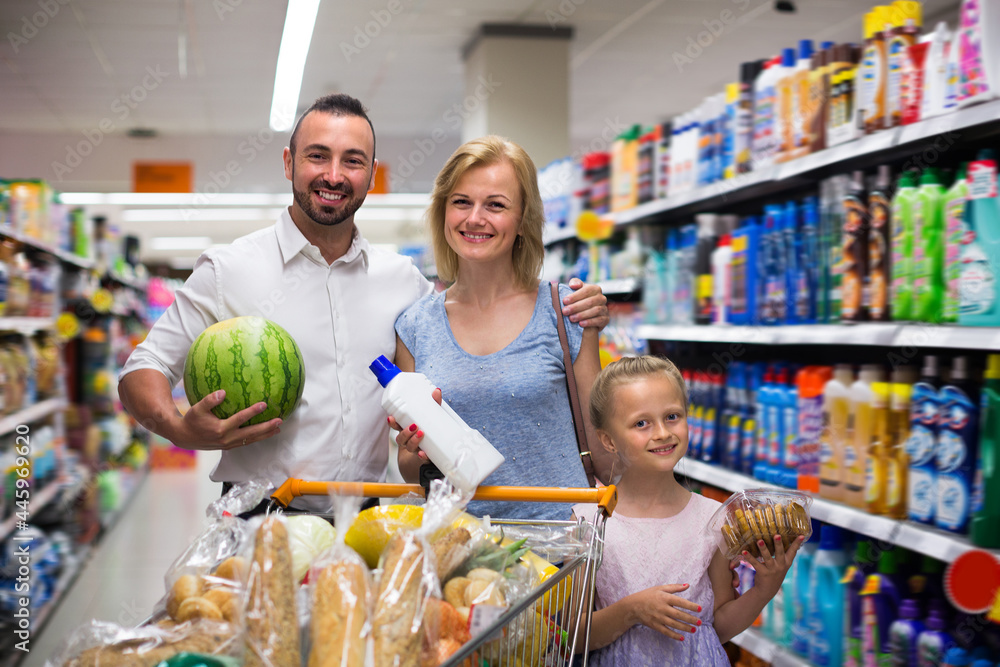 Mature parents with kid shopping in hypermarket and having full cart