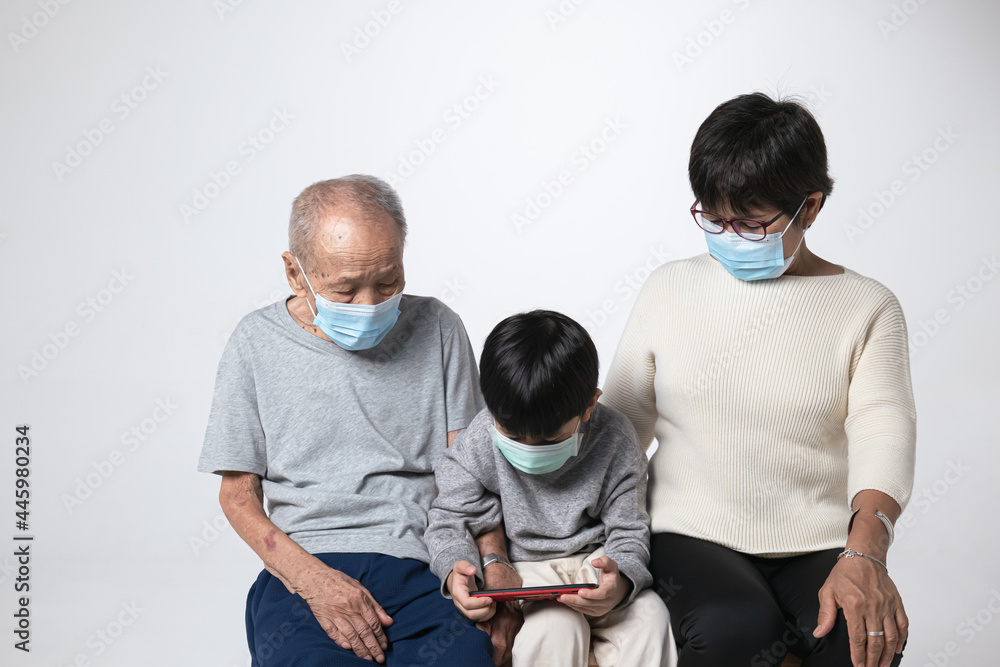 Senior Asian man with surgical face mask watching smartphone screen with his grandson and family. A 95 years old guy doing a video call due to the covid-19 virus pandemic. Senior Asian man with surgical face mask watching smartphone screen with his grandson and family. A 95 years old guy doing a video call due to the covid-19 virus pandemic.