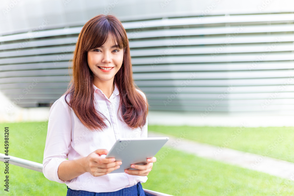 Fototapeta premium Happy young attractive business woman in her pink shirt using her tablet computer to check her social media outside of her office building