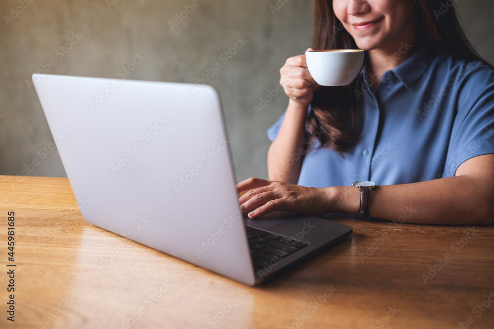 Closeup image of a young woman drinking coffee while working on laptop computer Closeup image of a young woman drinking coffee while working on laptop computer