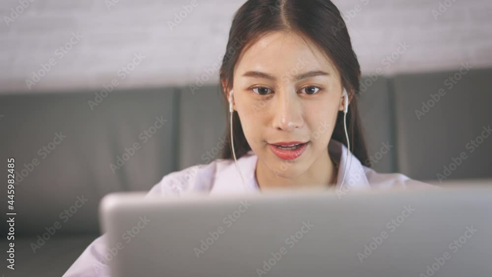 Successful young Asian female doctor with labcoat and earphones doing video conference call for consultation with patient from home at late night Successful young Asian female doctor with labcoat and earphones doing video conference call for consultation with patient from home at late night