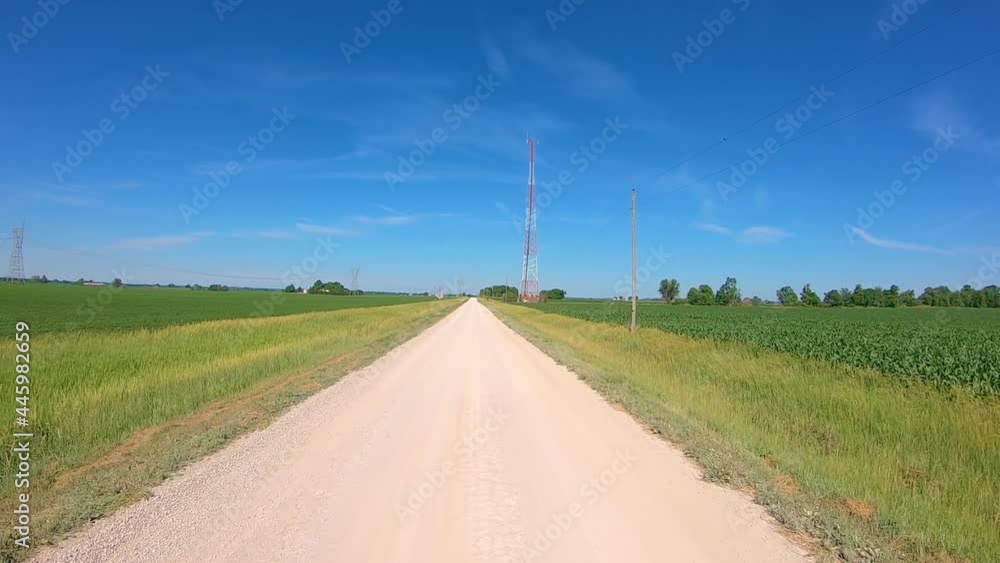 POV while driving on a gravel road and turns into a dirt lane; driving past a cell tower and fields POV while driving on a gravel road and turns into a dirt lane; driving past a cell tower and fields