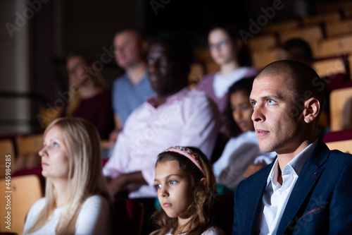 Portrait of adult man sitting in theater hall, absorbed in watching stage performance