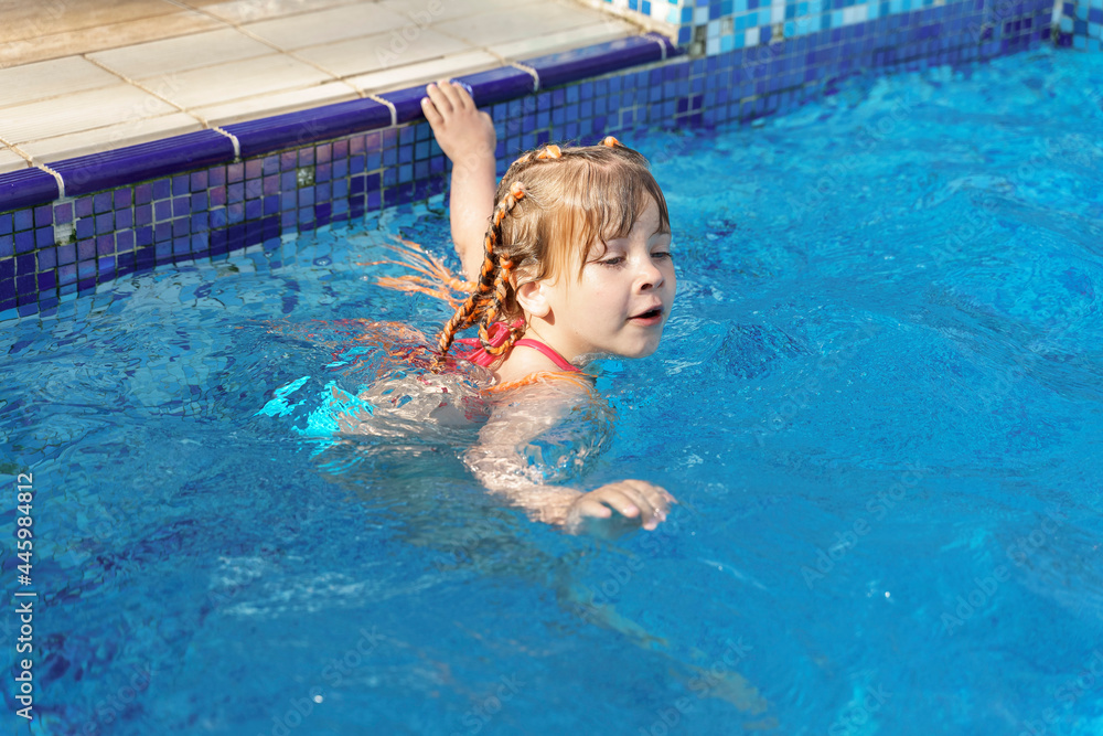 little girl swims in a swimming pool with blue water on a summer day little girl swims in a swimming pool with blue water on a summer day