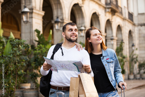 Portrait of happy young tourists with package walking with map at street