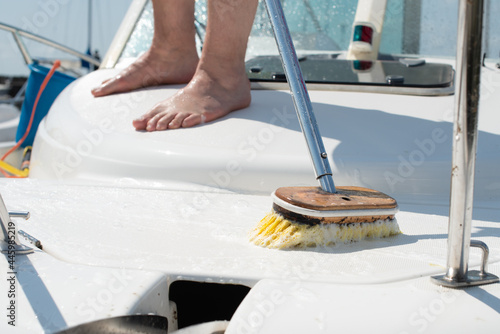 Man washing white boat with brush and pressure water system at pier.